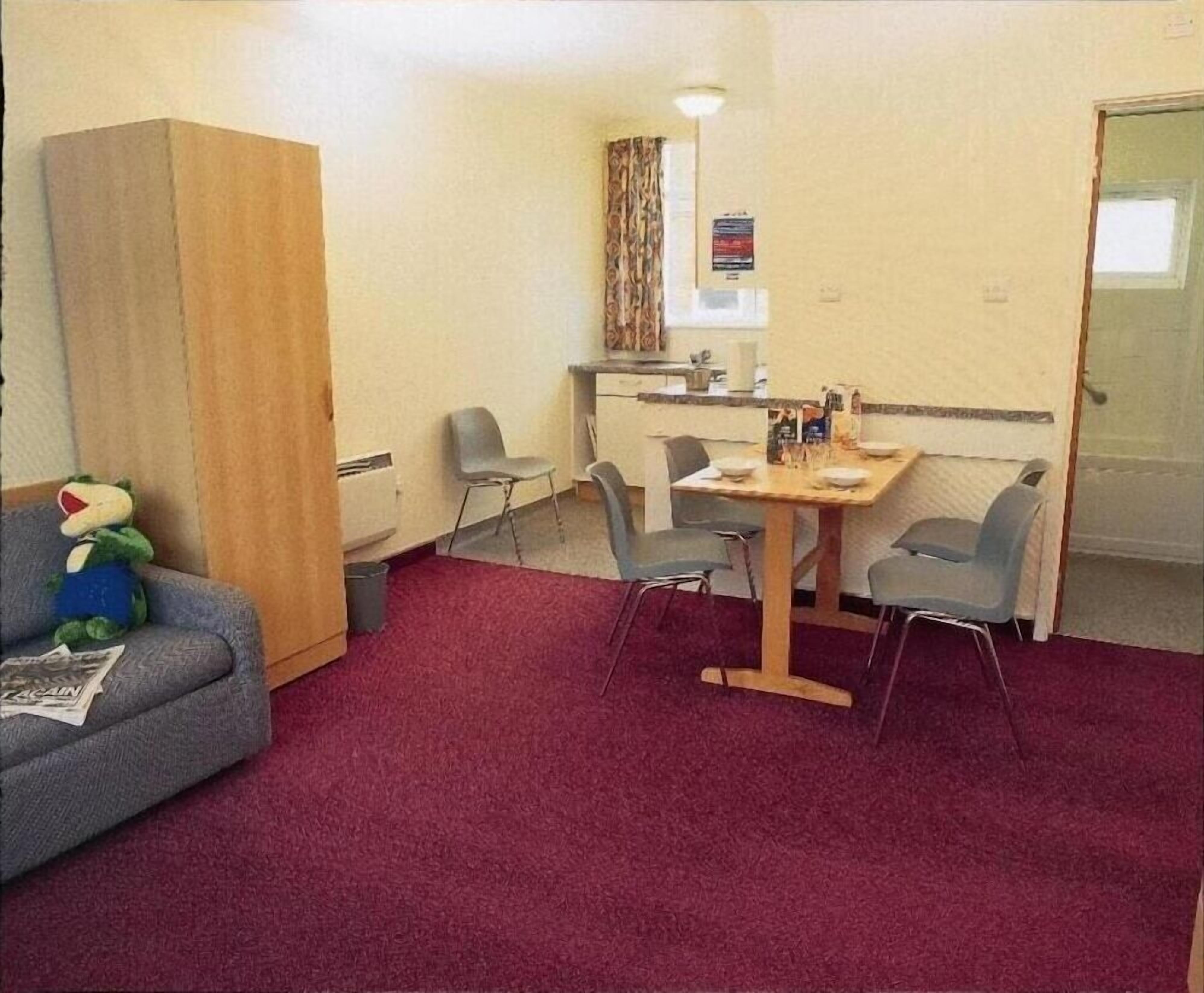 A small room with a wooden table, four chairs, a sofa, and a teddy bear.