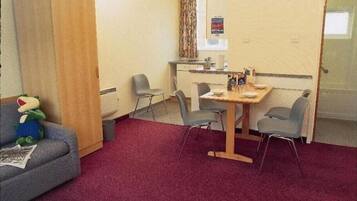 A small room with a wooden table, four chairs, a sofa, and a teddy bear.