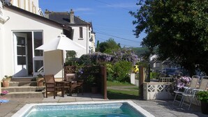 A swimming pool with a patio area, including a table and chairs, and a pergola with purple flowers. - Saffron House Hotel (Ilfracombe)