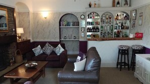 A cozy living room with a leather sofa, a coffee table, and a bar area with shelves of bottles and glasses. - Saffron House Hotel (Ilfracombe)