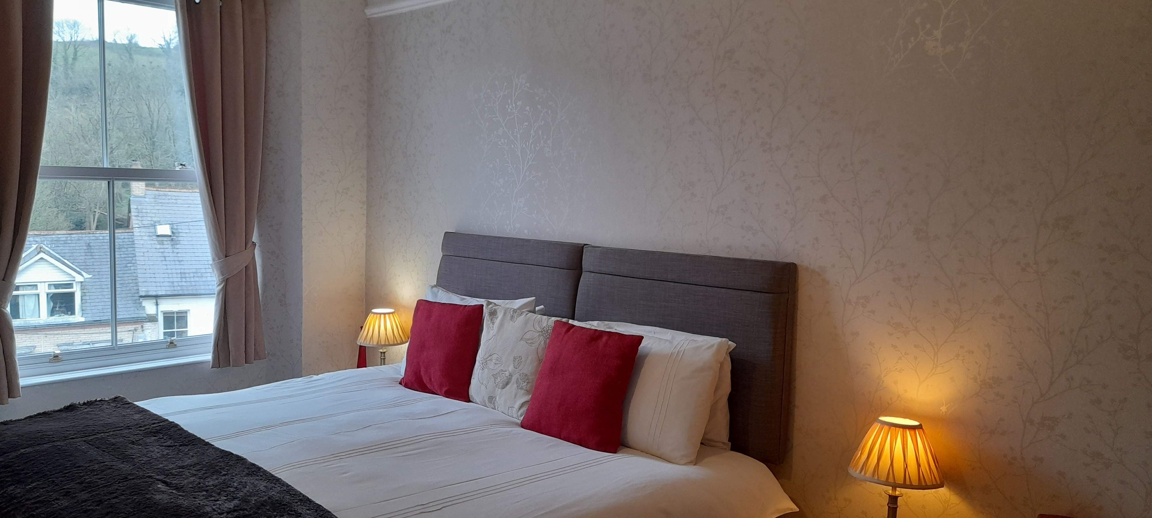 Een hotelkamer met een bed, twee bedlampen en een raam met gordijnen.