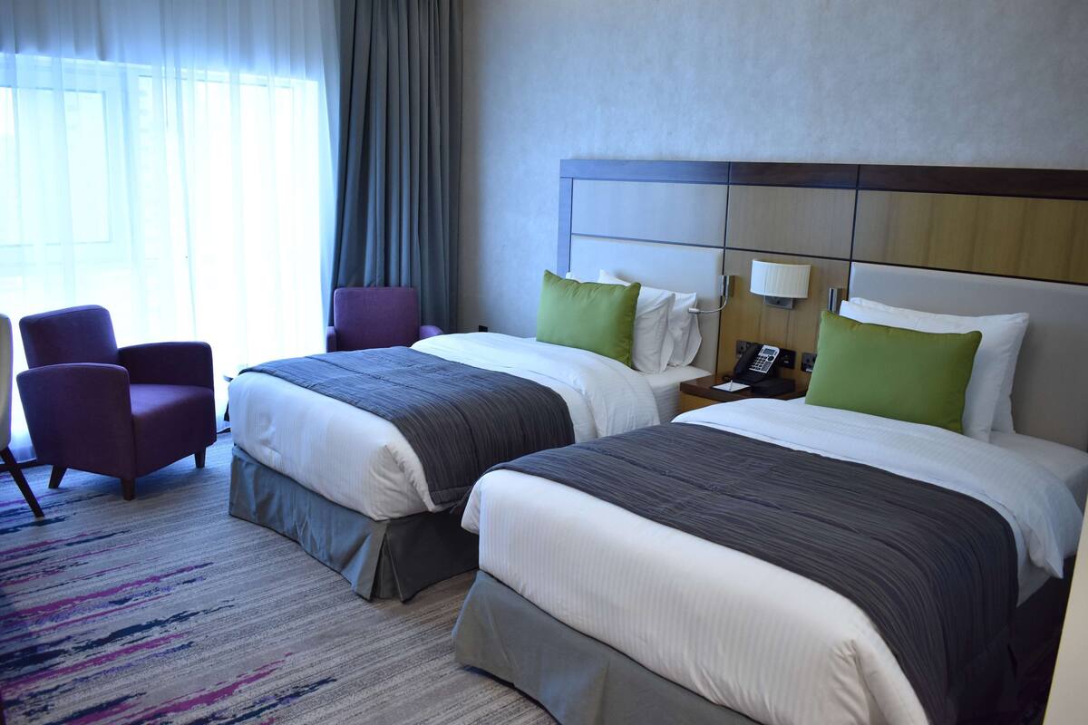 A hotel room with two beds, a chair, a nightstand, and a telephone.