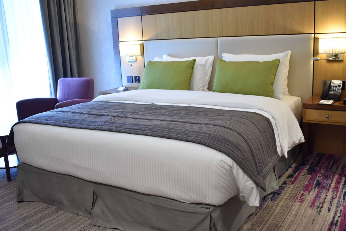 A hotel room with a large bed, a chair, a bedside table with a phone, and a lamp.