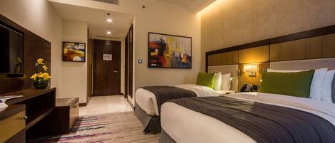 Una habitación de hotel con dos camas, un escritorio, un televisor y obras de arte en las paredes.