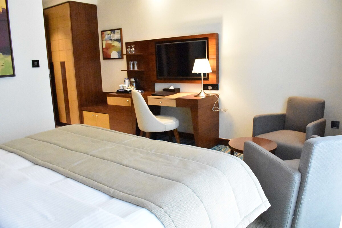 A hotel room with a bed, a desk, a chair, and a TV.