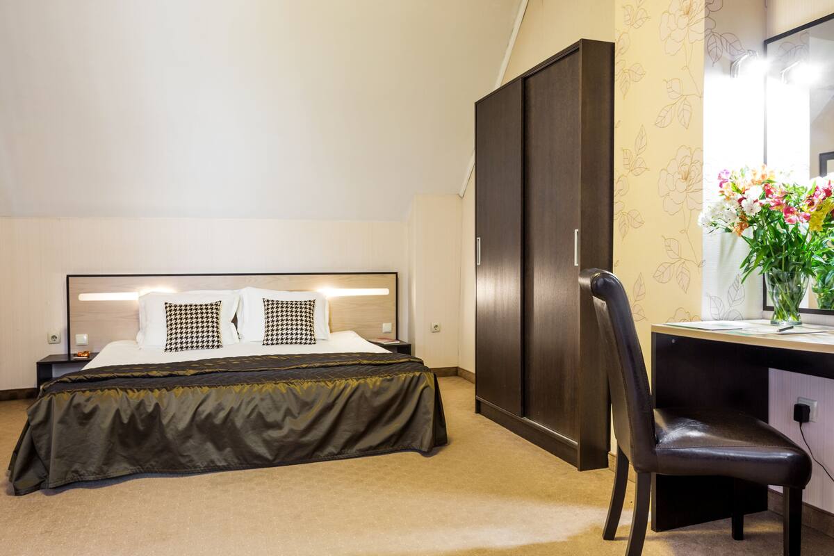 Una habitación de hotel con cama, escritorio, silla, armario y espejo.