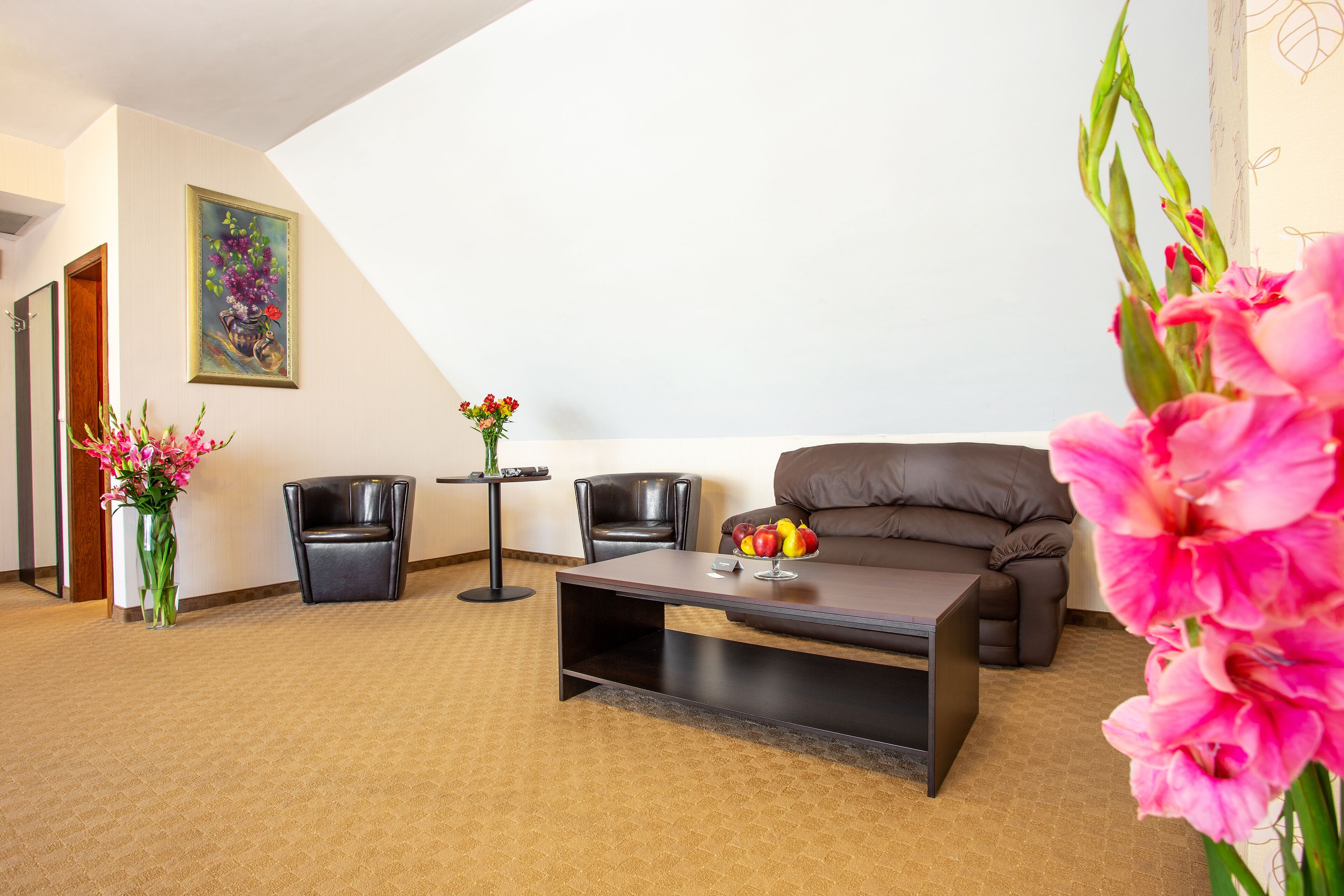 Una sala de estar moderna con un sofá marrón, dos sillas negras, una mesita de centro y un jarrón con flores rosadas.