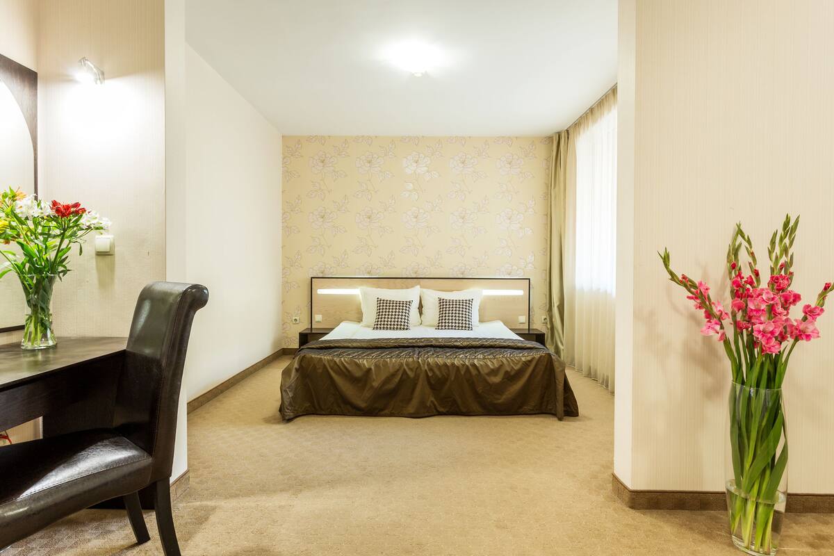 Una habitación de hotel con una cama, un escritorio y dos jarrones de flores.