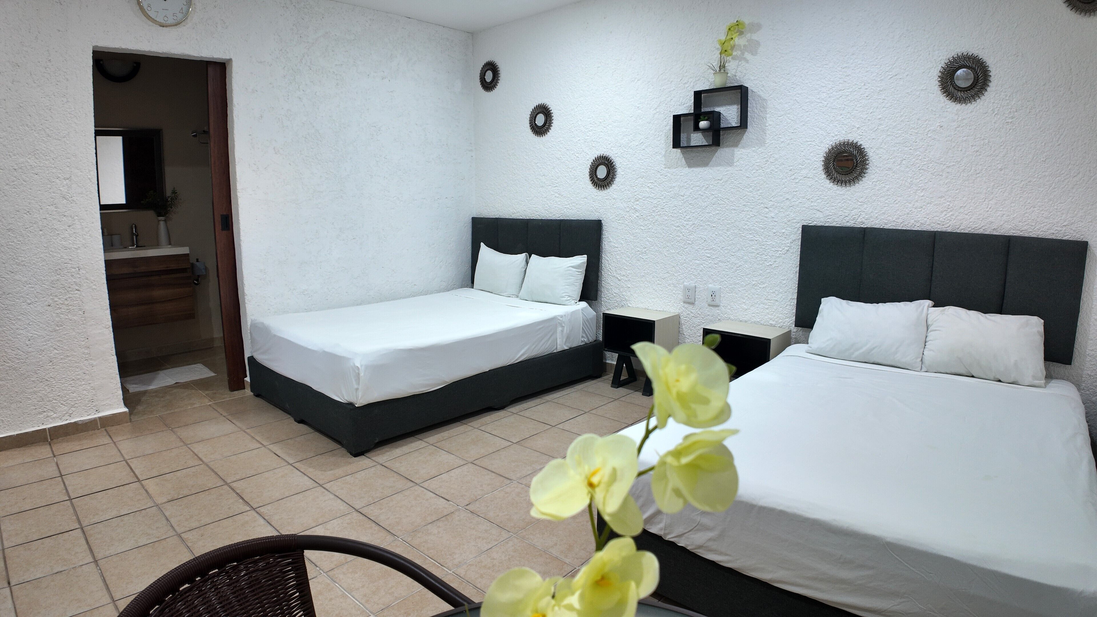 Habitación de hotel con dos camas individuales, una pequeña zona de estar y un baño visible a través de una puerta abierta.