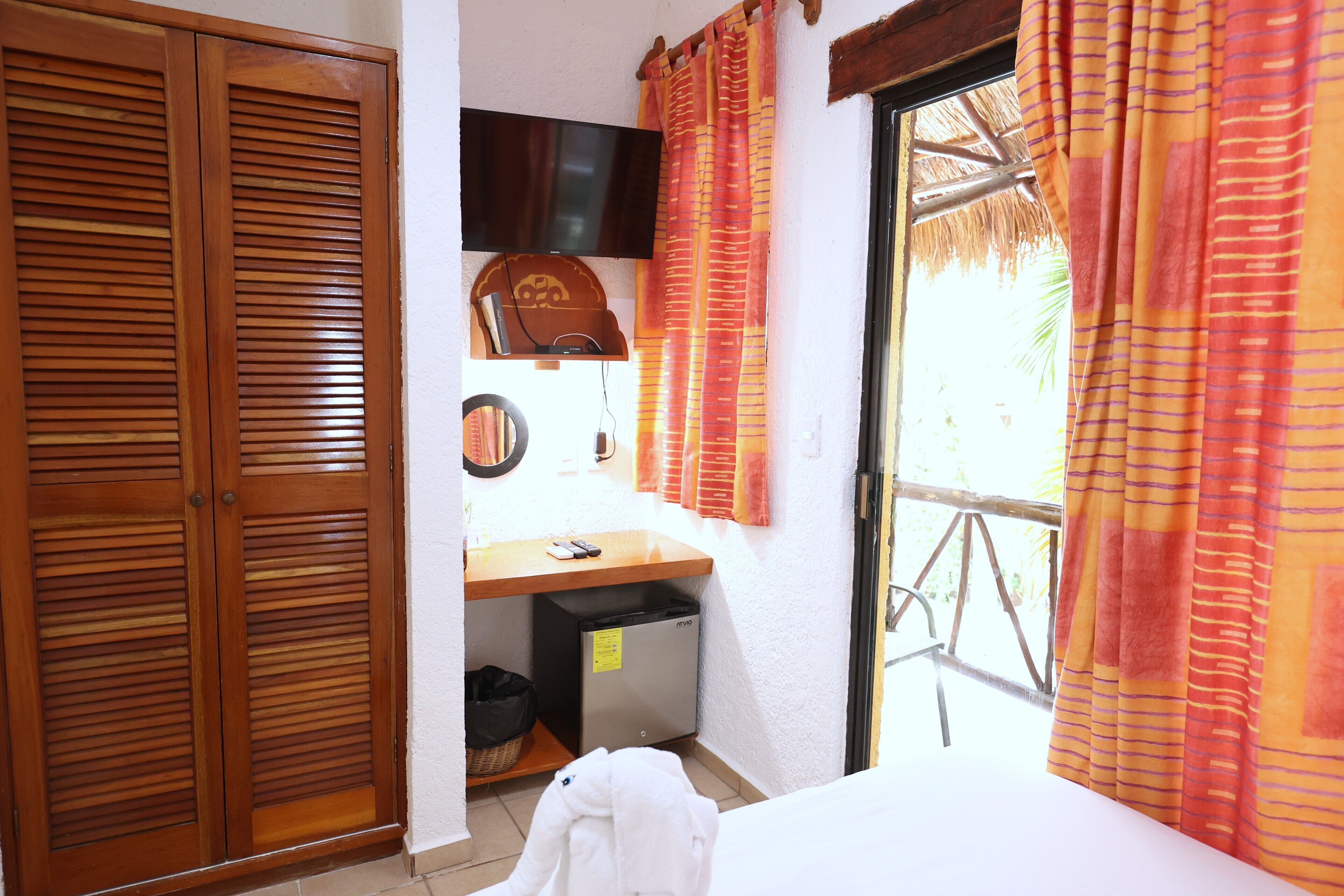 Habitación de hotel con contraventanas de madera, un escritorio con televisor y vistas a palmeras.