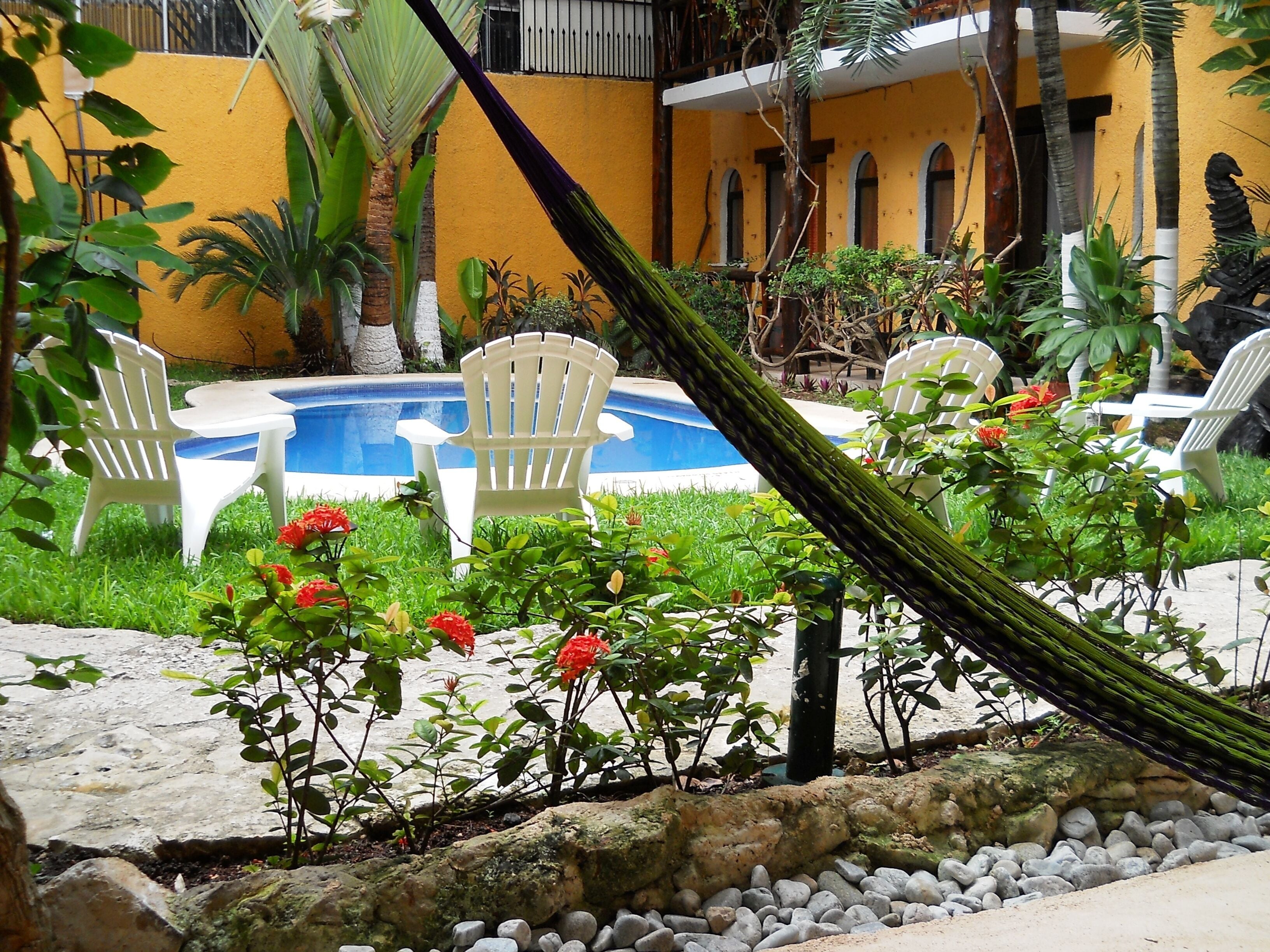 Un área de piscina con sillas blancas, una hamaca y flores rojas.