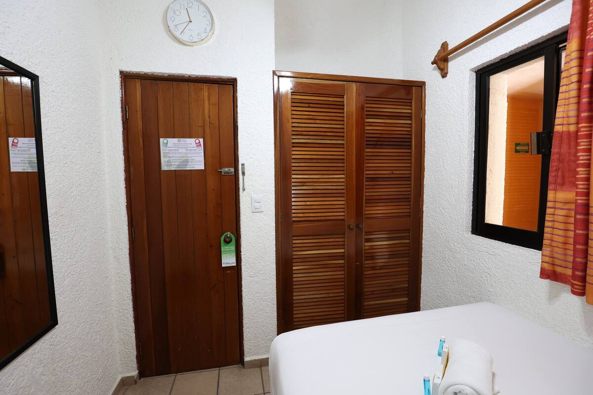 Habitació d'hotel amb un llit, una porta de fusta, un armari de fusta i un rellotge a la paret.