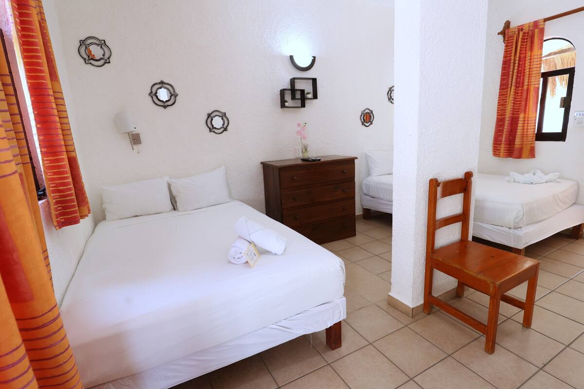 Habitació d'hotel amb un llit, una cadira de fusta, una petita taula de nit i una taula petita amb un vas.