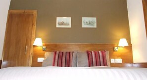 A hotel room with a wooden headboard, two wall-mounted lamps, a bed with striped pillows, and two framed pictures on the wall. - Leith House (Edinburgh)