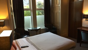 Una habitación de hotel con una cama grande, un escritorio, una silla, una mesita y un armario.