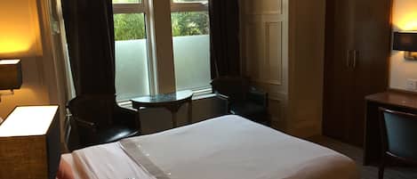 Quarto de hotel com uma cama grande, uma escrivaninha, uma cadeira, uma mesinha e um guarda-roupa.