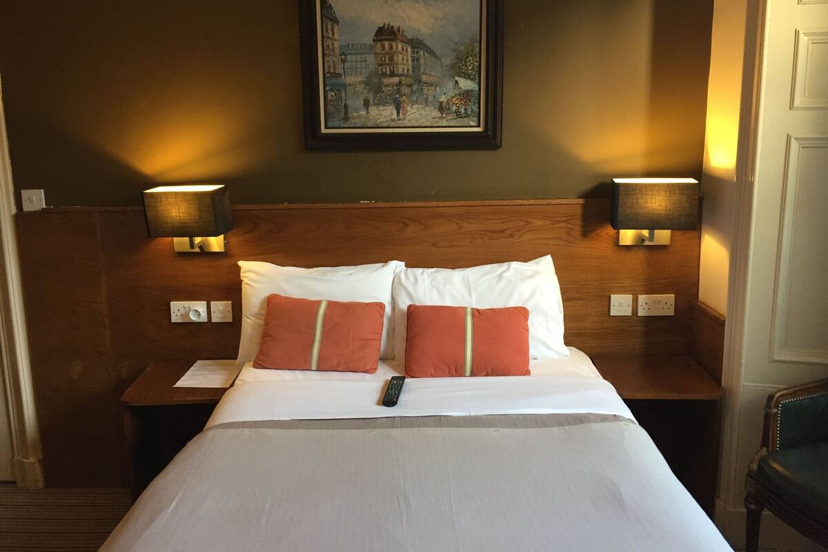 A hotel room with a large bed, two nightstands with lamps, a painting on the wall, and a chair.