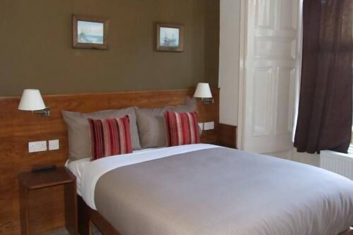 A hotel room with a bed, two bedside lamps, a nightstand, and two framed pictures on the wall.