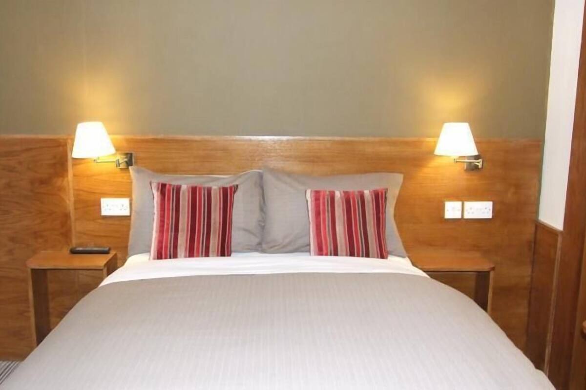 A hotel room with a wooden headboard, two bedside lamps, a bed with white bedding, and two striped pillows.