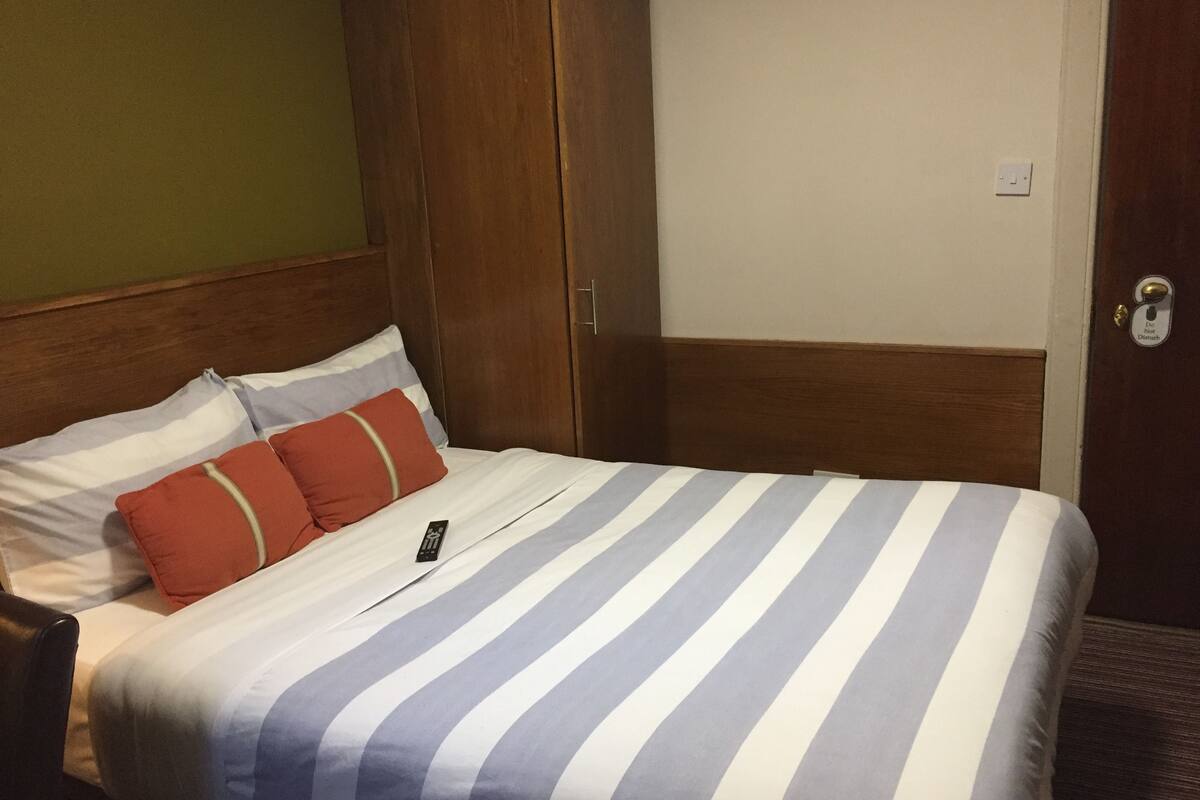 A hotel room with a bed, a wooden wardrobe, and a door with a lock.