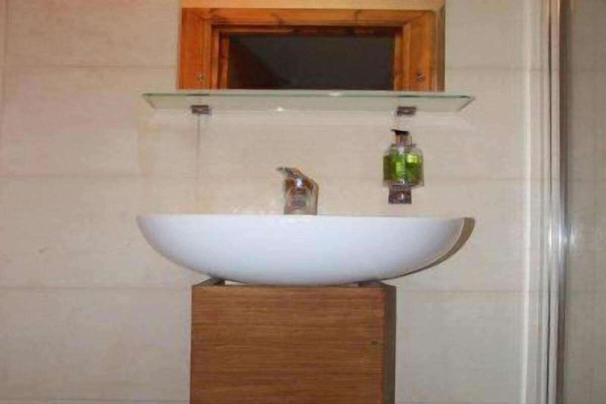 A bathroom with a white vessel sink, wooden base, glass shelf above, and a mirror with a wooden frame.