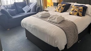 Quarto de hotel com cama, mesa de cabeceira, abajur e sofá.