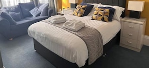 A hotel room with a bed, a nightstand, a bedside table, a lamp, and a sofa. - Hotel Catania (Scarborough)