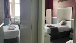 Quarto de hotel com duas camas, um guarda-roupa e uma janela com cortinas.