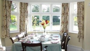 A dining room with a bay window, floral curtains, and a table set for four. - Church Farm (Solihull)