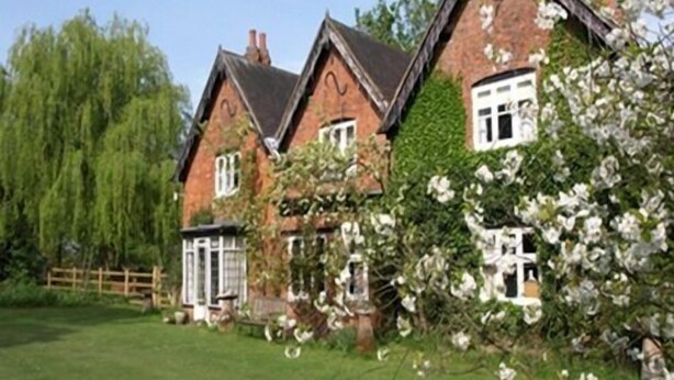 A traditional brick house with a gabled roof, surrounded by lush greenery and flowering plants. - Church Farm (Solihull)