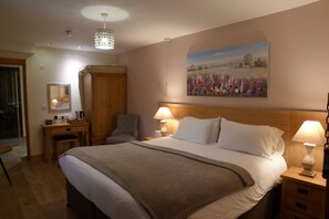 A neatly arranged bedroom with a large bed, bedside lamps, a wooden wardrobe, a desk with a chair, and a painting on the wall.