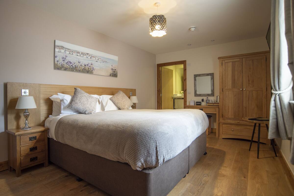 A bedroom with a large bed, wooden headboard, bedside tables, a nightstand, a hanging lamp, a wardrobe, and a mirror.