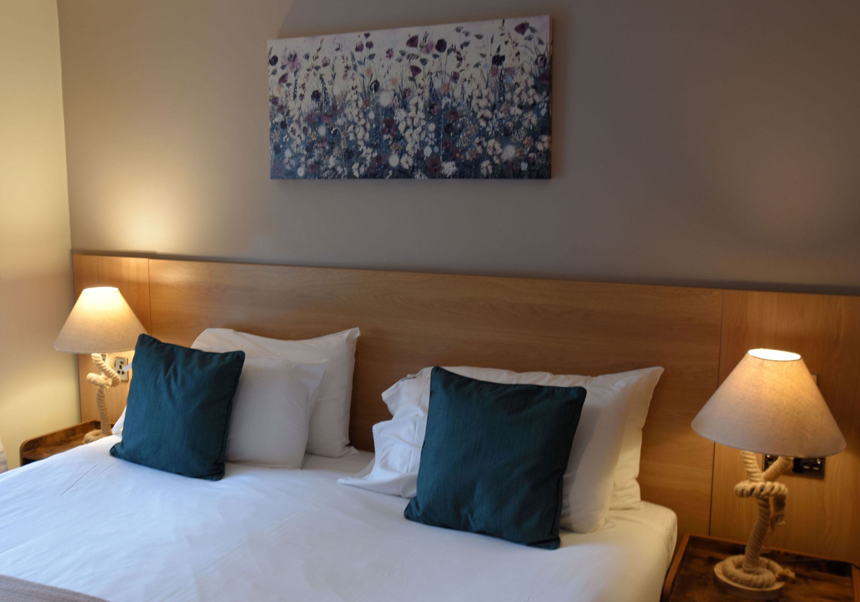 Habitació d'hotel amb un llit gran, dues làmpades de nit i una obra d'art floral a la paret.
