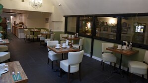 Un amplio comedor interior con varias mesas y sillas, un candelabro y vistas a través de grandes ventanales.