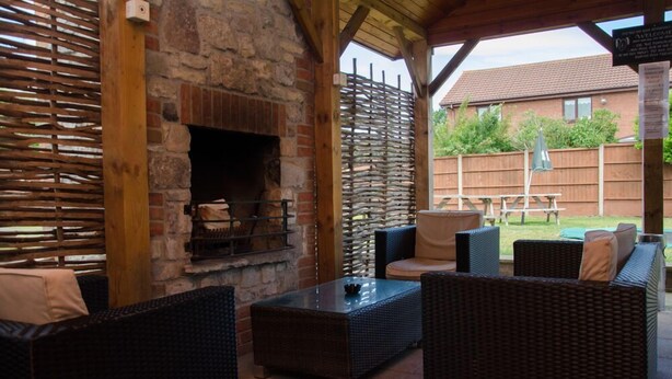 Un patio al aire libre con mobiliario de mimbre, una chimenea de piedra y una pérgola de madera.