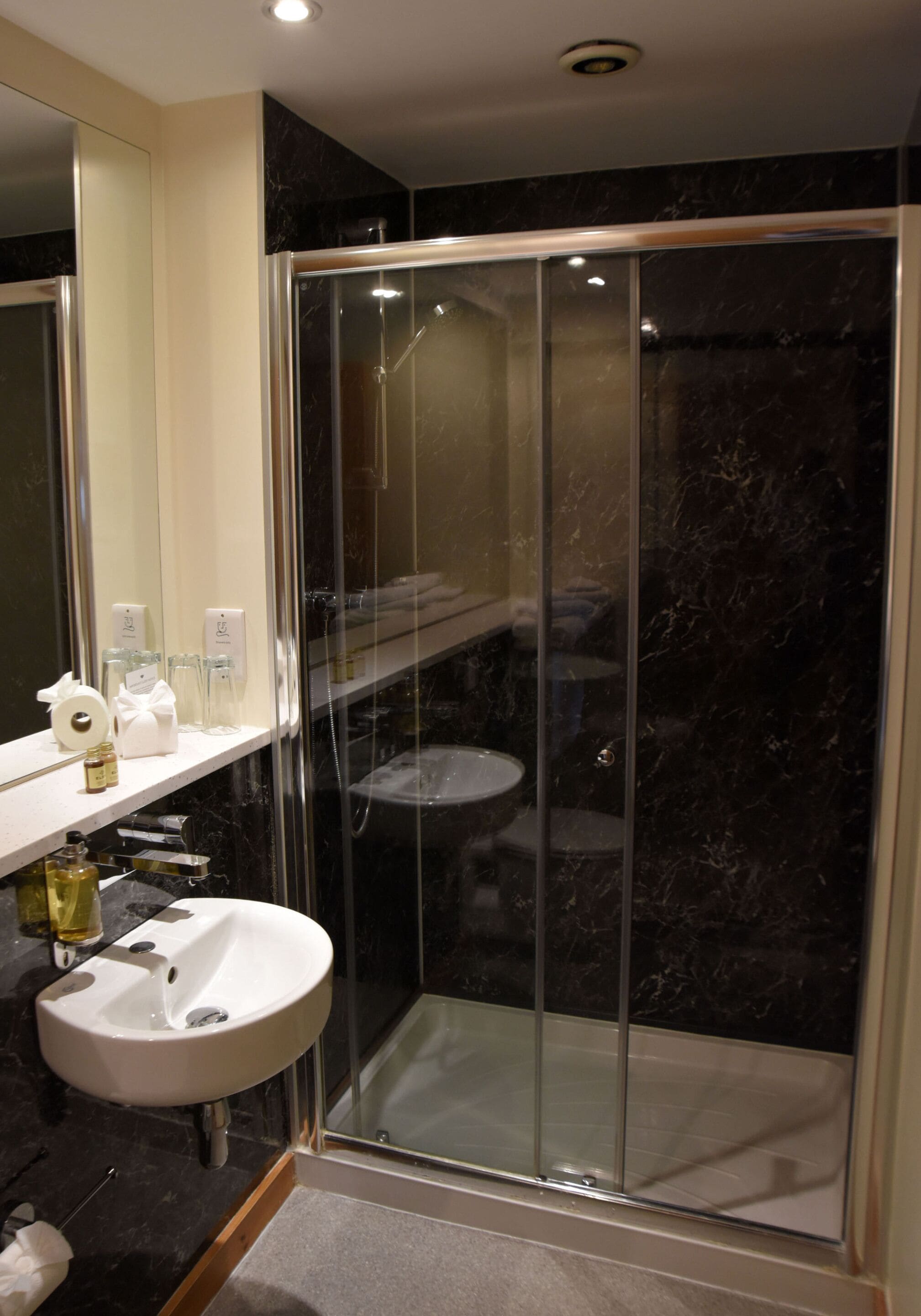Een moderne badkamer met een douchecabine van glas, een witte wastafel en een spiegel boven de wastafel.