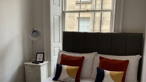 A neatly made bed with white and yellow bedding, two pillows, and folded towels on a yellow quilted bedspread. - Bide Collective (Edinburgh)