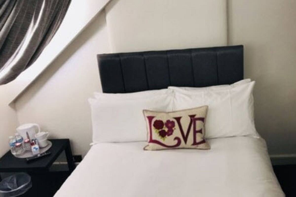 A hotel room with a bed, a pillow with the word "LOVE" on it, a bedside table with a lamp, and a small table with a cup and a tray.