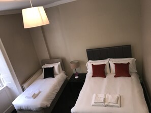 Two single beds with white linens and pillows, a nightstand with a lamp and decorative item, and a window.