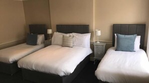 Three single beds with white duvets and matching pillows, flanked by nightstands with lamps.