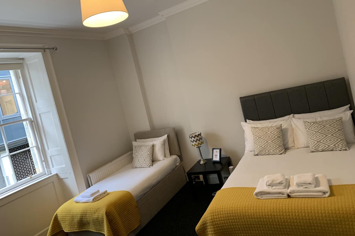 A hotel room with two beds, a bedside table, a window, and a hanging light fixture.