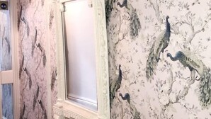 A wall with a floral wallpaper featuring peacocks and a decorative mirror with a ruffled frame. - Bide Collective (Edinburgh)