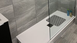A modern shower area with grey tiles, a glass-enclosed shower, a white towel, and a control panel. - Bide Collective (Edinburgh)