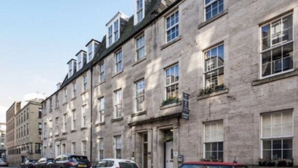 A row of stone buildings with multiple windows and a clear sky. - Bide Collective (Edinburgh)