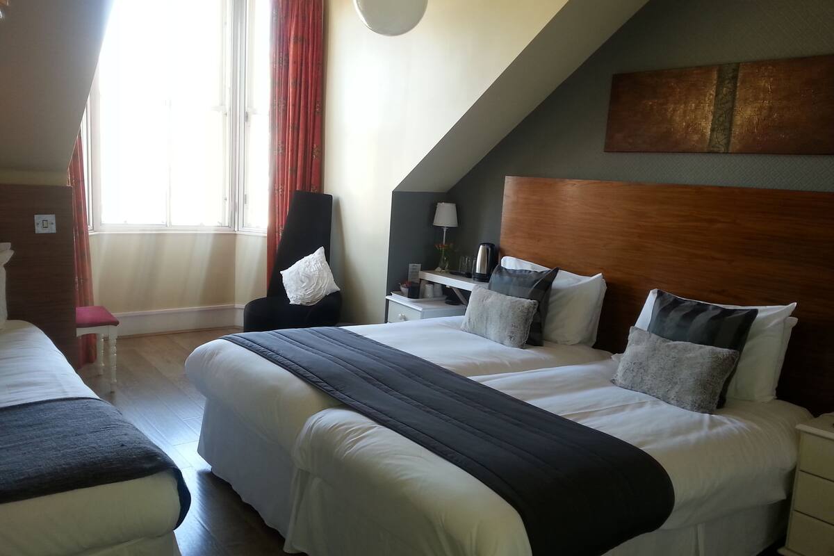 Quarto de hotel com duas camas, uma escrivaninha e uma cadeira.