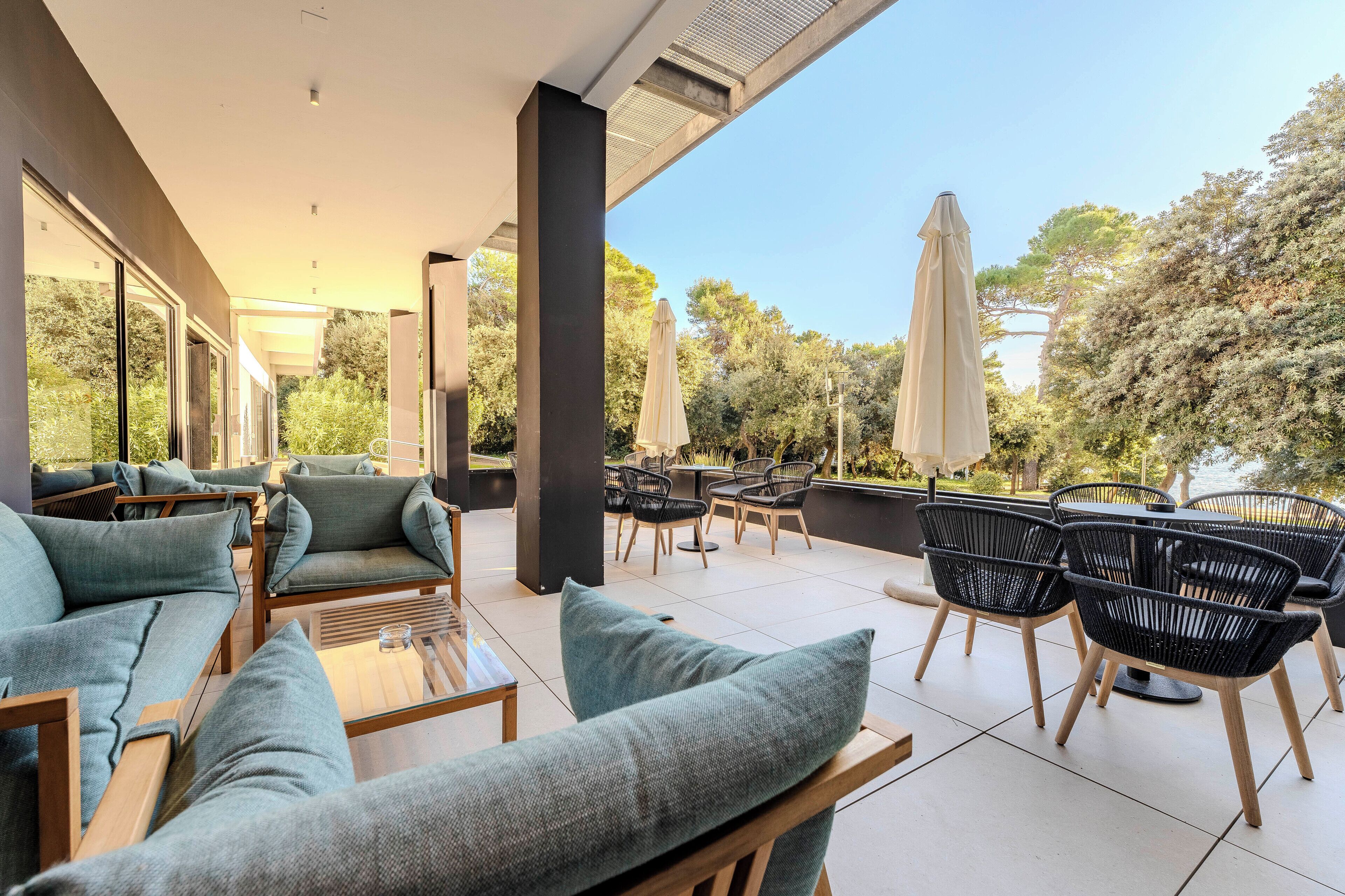 A modern outdoor seating area with sofas and chairs, a bar, and umbrellas.