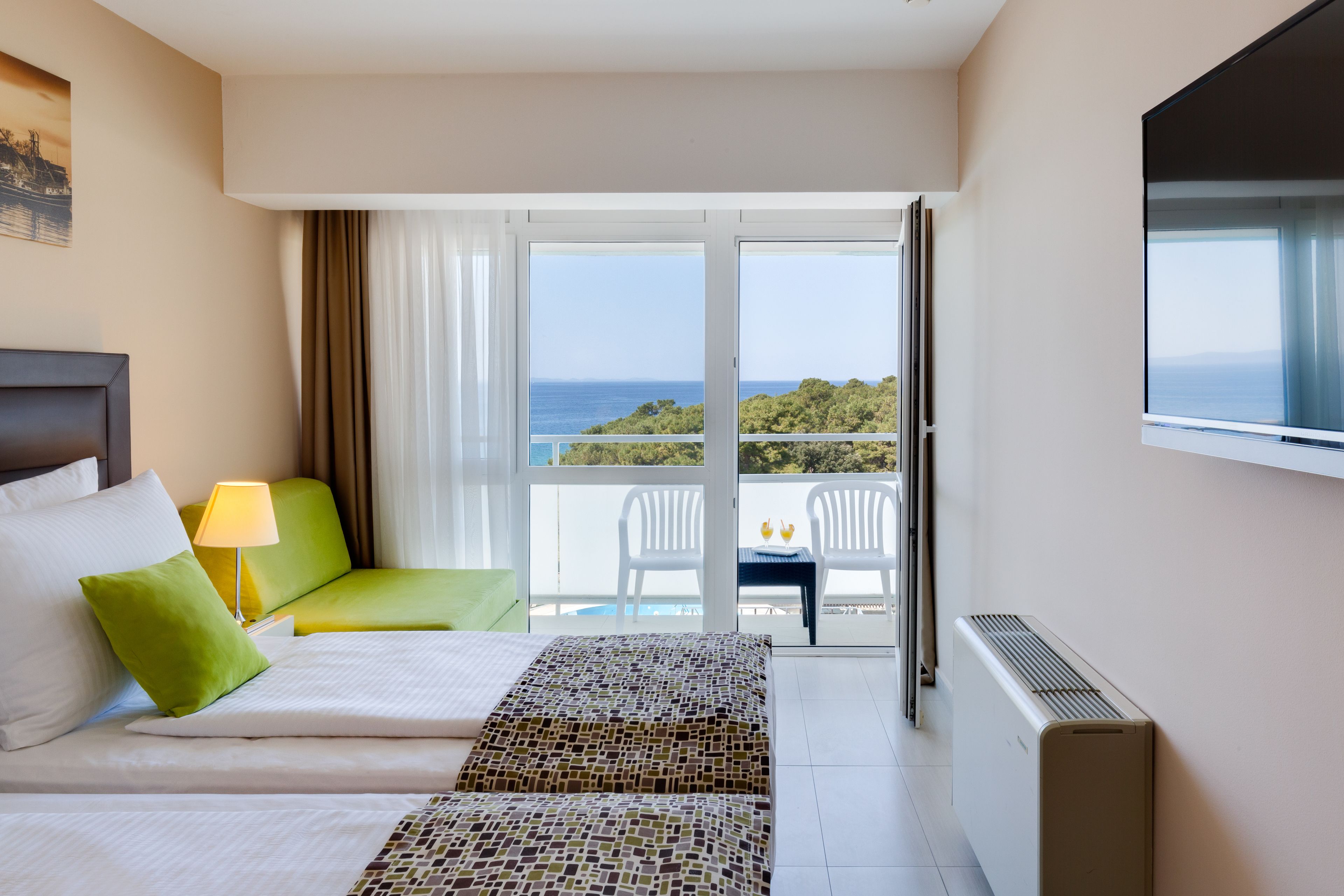 Habitación de hotel con cama, sofá, una mesa con dos bebidas y vista al mar.