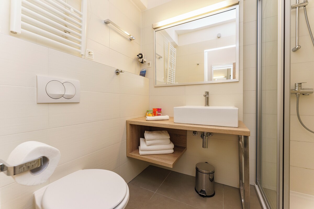 Un baño moderno con inodoro, lavamanos, espejo, ducha y un cubo de basura.