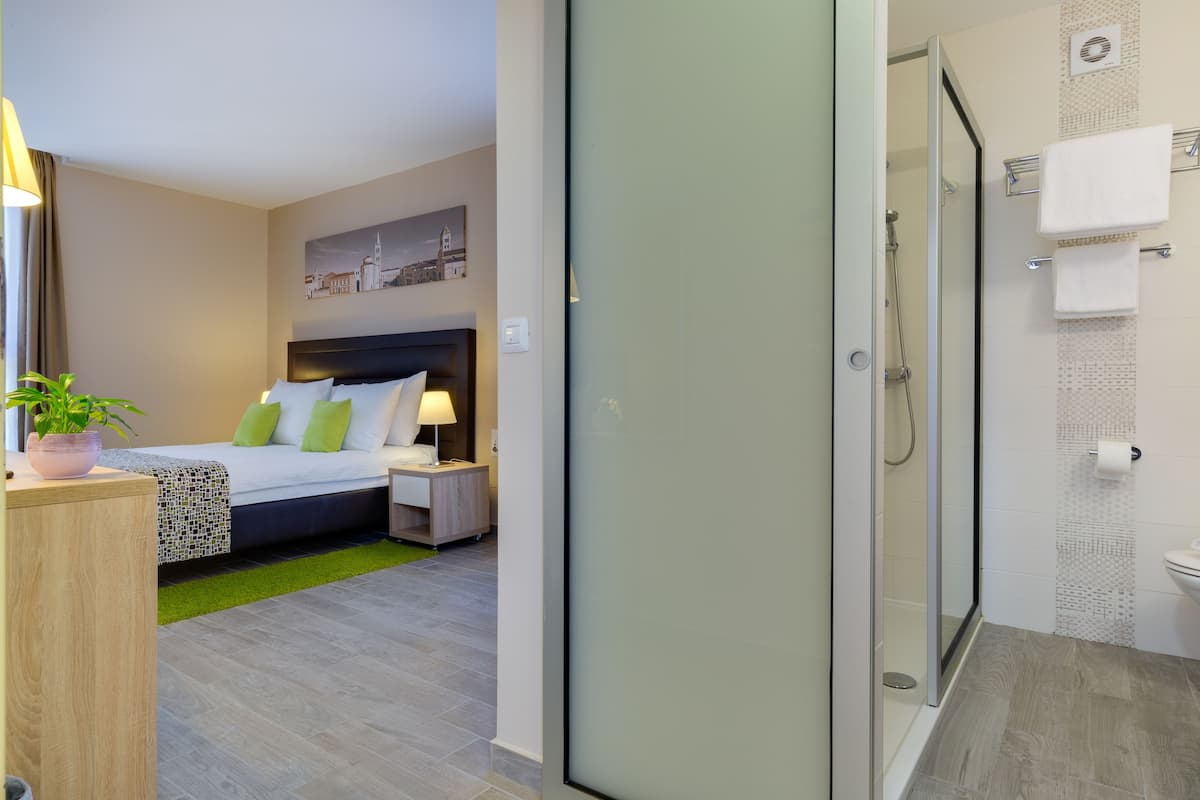 A hotel room with a bed, bedside table, lamp, and a view of the cityscape through the window.