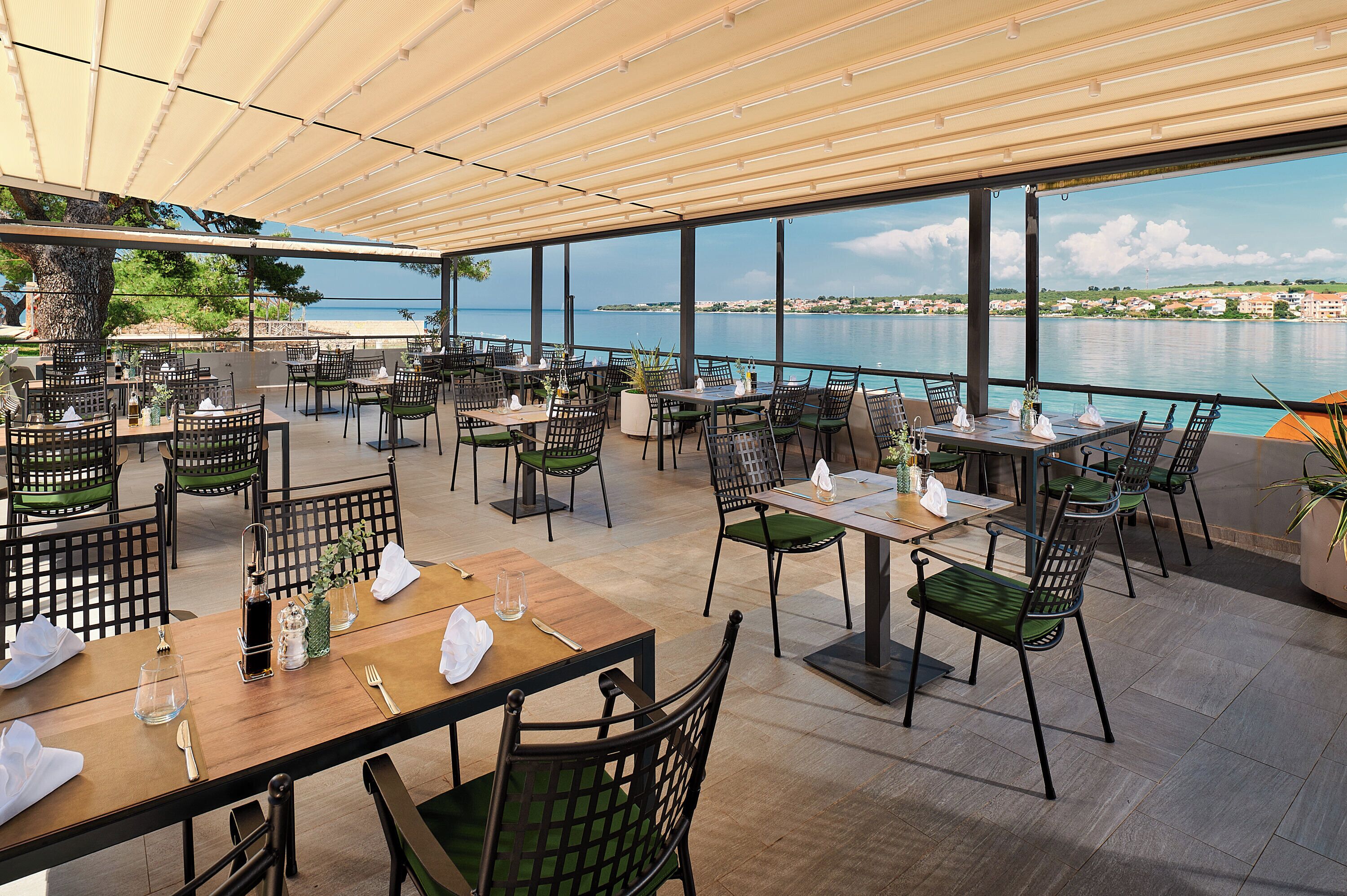An outdoor dining area with tables and chairs, overlooking a body of water and a distant shoreline.